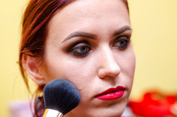 makijaż artysta ma makijaż do kobiety w salonie piękności. Zbliżenie twarzy modelki z makijażem. - Zdjęcie, obraz
