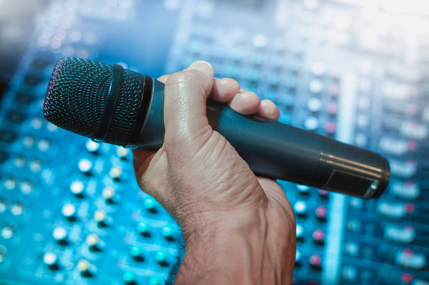 Singen mit einem drahtlosen Mikrofon, Sänger oder Sänger mit dem Hintergrund des Audio-Mischpults oder des blauen Soundtisches für Live-Auftritte und Musikkonzerte. - Foto, Bild
