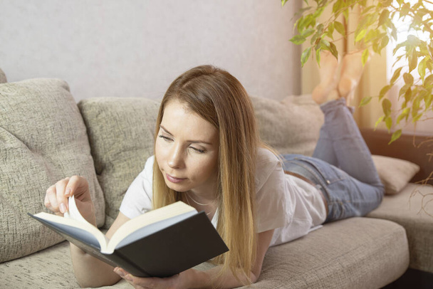 Happy young woman reading storybook on couch at home - Foto, Imagem