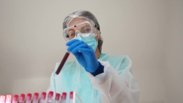 Doctor in the laboratory with a biological tube for analysis and sampling of Covid-19 infectious disea. Lab technician does a chemical blood test. Records the results - Πλάνα, βίντεο