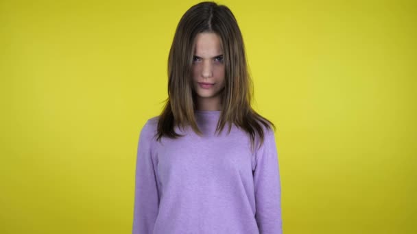 Angry teenager girl in a pink sweater laughing on a yellow background - Video