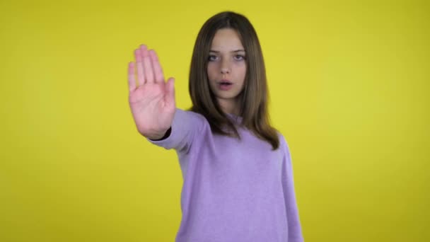 Teenager girl raises her hand with a palm and says stop on yellow background - Footage, Video
