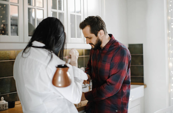 husband and wife in pajamas are kidding and making coffee in a stylish kitchen, interior design - Foto, afbeelding