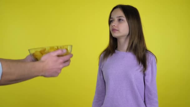 Teen girl refuses potato chips in a glass bowl shaking hands and head - Video