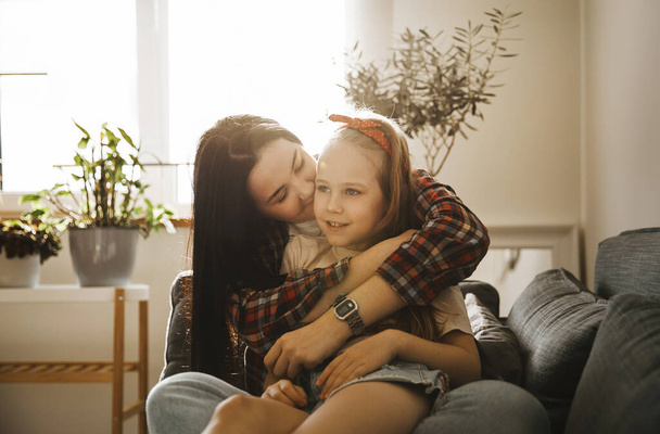 cute brunette mom in a plaid shirt and daughter hugging and having fun in a stylish living room at home - Foto, Imagen