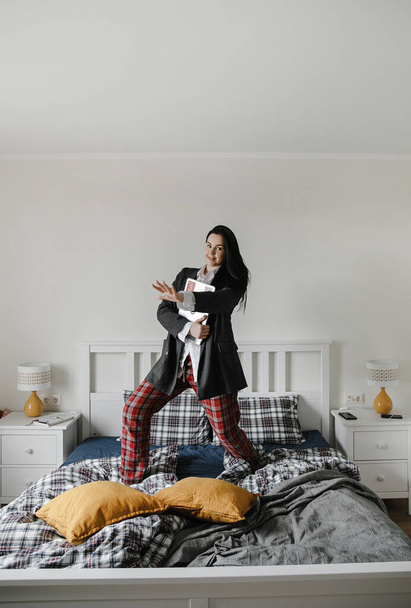 businesswoman in pajamas and jacket works at a computer in her checkered bed, bedroom interior design - Photo, image