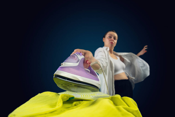 Close up of young caucasian woman ironing bright clothes with expressive emotions in action, motion - Foto, Bild