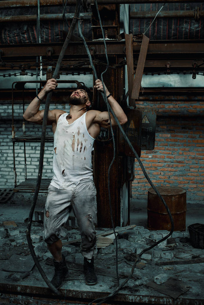Arbeiter, der in einer Fabrik arbeitet, Elektrizität verlegt, zerrissene Arbeitsgestalt, Sportfigur in einem Kerl - Foto, Bild