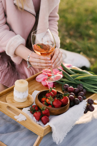 Picnic basket with strawberries, grapes and buns on the green grass in the garden - Фото, изображение