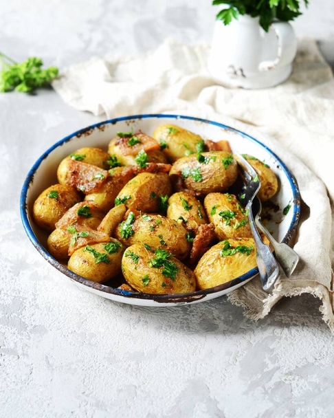 Jonge gebakken aardappel met spek, specerijen en kruiden in een bakvorm op een grijze achtergrond, stilleven - Foto, afbeelding