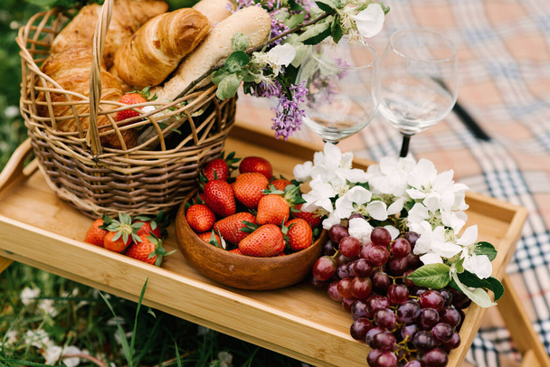 Καλάθι πικνίκ με φράουλες, σταφύλια και ψωμάκια στο πράσινο γρασίδι του κήπου - Φωτογραφία, εικόνα