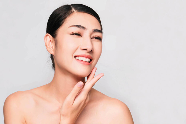 young beautiful asian woman with clean and bright skin, Cosmetic Beauty Concept,hands touch on the cheek, smiling and friendly face isolated on grey background - Fotoğraf, Görsel