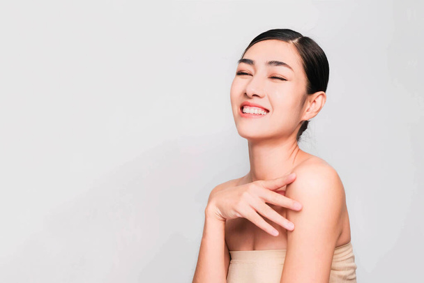 young beautiful asian woman with clean and bright skin, Cosmetic Beauty Concept,hands touch on the cheek, smiling and friendly face isolated on grey background - Foto, Imagem