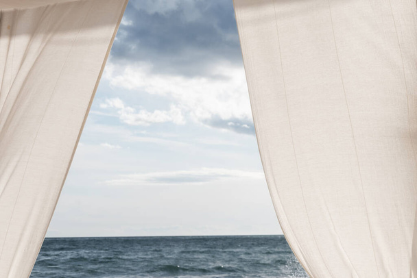View of the sea between white curtains and white and blue clouds sky - Foto, Imagen