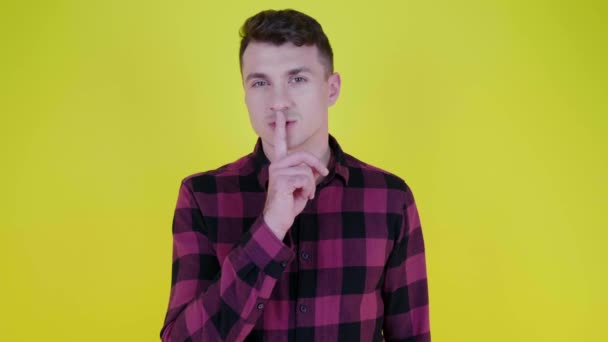 Zwijg. Man in roze geruite shirt zet wijsvinger op lippen op gele achtergrond - Video