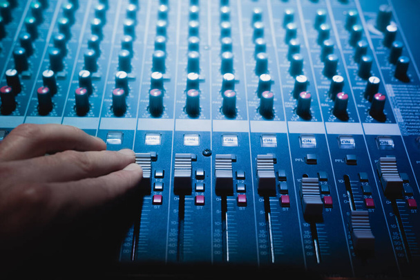 mit Audio-Mixer. Drehen Sie die Lautstärke mit der Hand auf einen Soundtisch. DJ, Tontechniker oder Musikproduzent, der im Tonstudio mit blauem Neon-Discolicht Musik produziert. - Foto, Bild