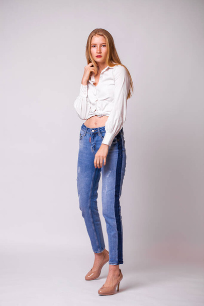 Full body portrait of a young beautiful blonde woman in blue jeans. Studio gray isolated background - Foto, Imagem