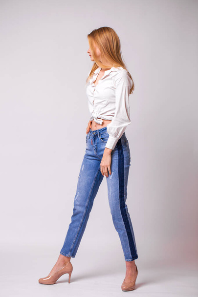 Full body portrait of a young beautiful blonde woman in blue jeans. Studio gray isolated background - Fotoğraf, Görsel