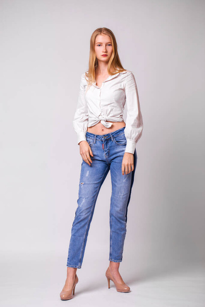 Full body portrait of a young beautiful blonde woman in blue jeans. Studio gray isolated background - Fotografie, Obrázek