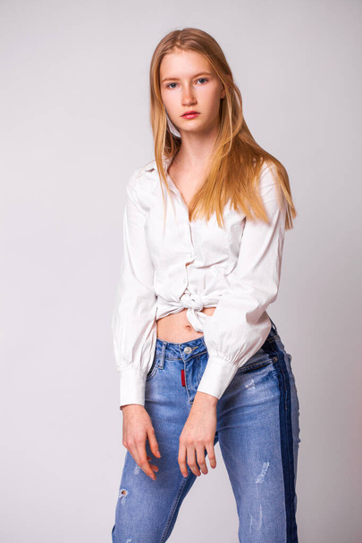 Closeup portrait of a young beautiful blonde woman in a white shirt. Studio gray isolated background - 写真・画像