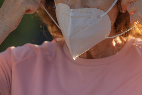 Prawdziwa kobieta pokazuje, jak założyć maskę ochronną, aby zapobiec rozprzestrzenianiu się wirusa COVID-19 na innych ludzi podczas spaceru ulicą w dzielnicy Retiro w Madrycie, Hiszpania. - Zdjęcie, obraz