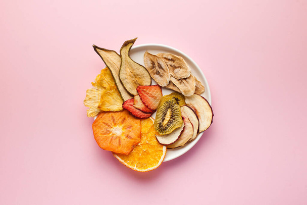  Dried fruit chips on a pink background. The concept of a healthy snack without sugar, dessert for vegetarians. Copy space. Flatlay - Фото, зображення
