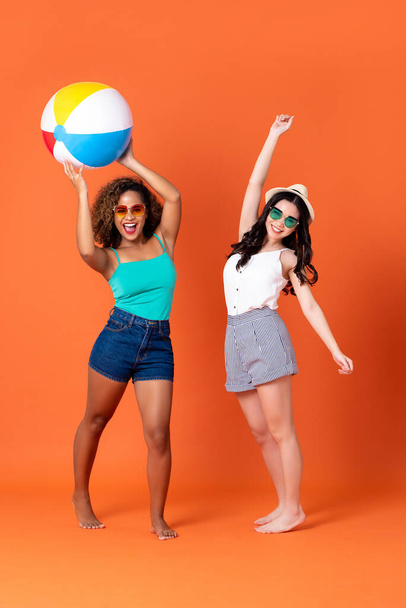 Happy African American and Asian woman friends in casual summer clothes with colorful beach ball in coral orange background - Foto, Bild