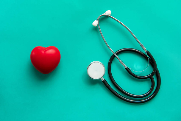 Rode hartvormige bal met stethoscoop op groene achtergrond, gezondheidszorg en medisch concept - Foto, afbeelding