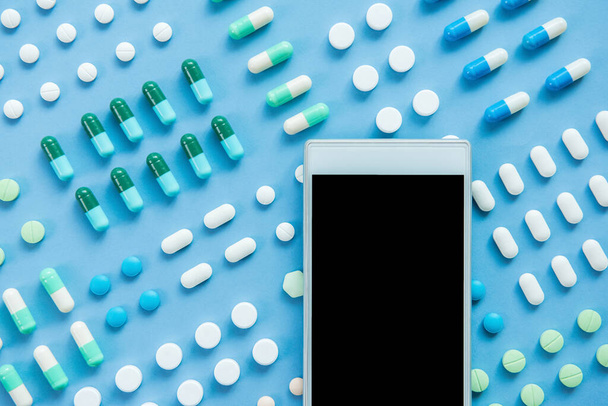 Verschillende soorten medische pillen en medicijnen met leeg scherm mobiele telefoon voor uw teksten, bovenaanzicht op lichtblauwe achtergrond - Foto, afbeelding