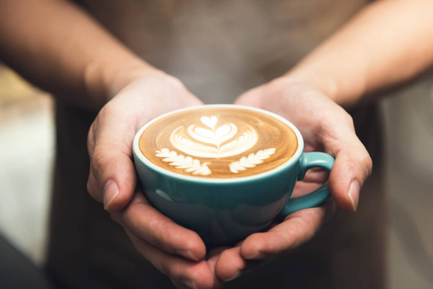 表面に美しいロゼッタ・ラテのアートパターンを提示コーヒーのカップを保持バリスタの手 - 写真・画像