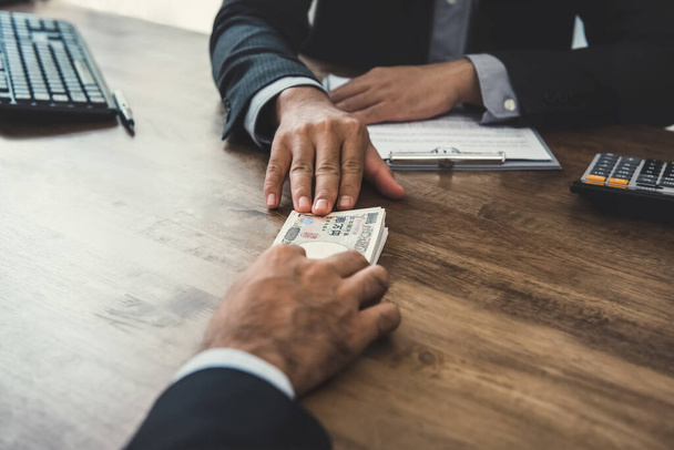 Podnikatel dává peníze, japonské jenové bankovky, svému partnerovi u stolu při uzavírání kontraktu - úvěry, úplatky a korupce - Fotografie, Obrázek