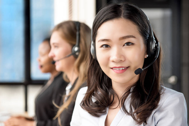 Hymyilevä kaunis aasialainen nainen telemarkkinointi asiakaspalvelu agentti työskentelee call center hänen monikansallinen joukkue
 - Valokuva, kuva