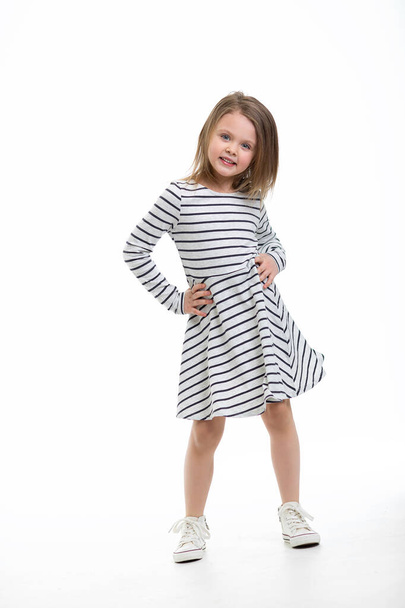 Cute pretty little blonde girl with a mischievous cute full-length smile standing on isolated white background. Casual clothes. Look at the camera. Copy pace for text. - Foto, imagen