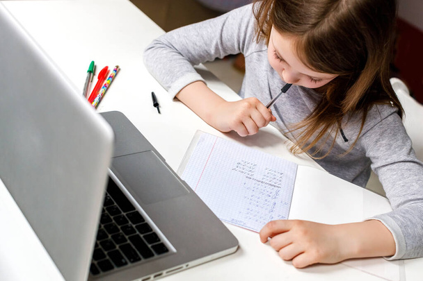 Η μαθήτρια κάνει τα μαθήματά της σε ένα σημειωματάριο με φορητό υπολογιστή στο σπίτι. Κατ 'οίκον διδασκαλία, εξ αποστάσεως εκπαίδευση, κατ' οίκον διδασκαλία, σπουδές online εκπαίδευσης κατά τη διάρκεια της καραντίνας. - Φωτογραφία, εικόνα
