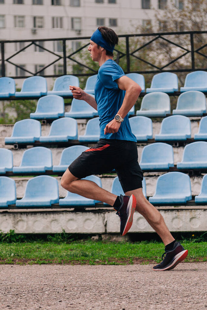 A young athlete in a blue T-shirt runs around the stadium - Foto, imagen
