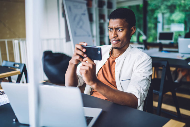 African American male student puzzled with web information on university website photographing laptop screen for sending media sms to colleagues and discuss mistakes, user of modern technology - Foto, imagen
