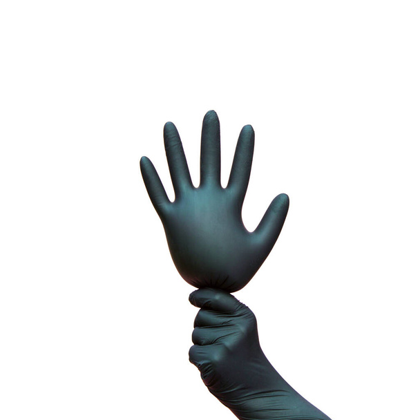ένα χέρι σε ένα μαύρο χειρουργικό γάντι κρατά το φουσκωμένο γάντι σαν μπαλόνι. Απομονωμένο σε λευκό φόντο. Το σύμβολο του εορτασμού της νίκης επί των κορωνοϊών. - Φωτογραφία, εικόνα