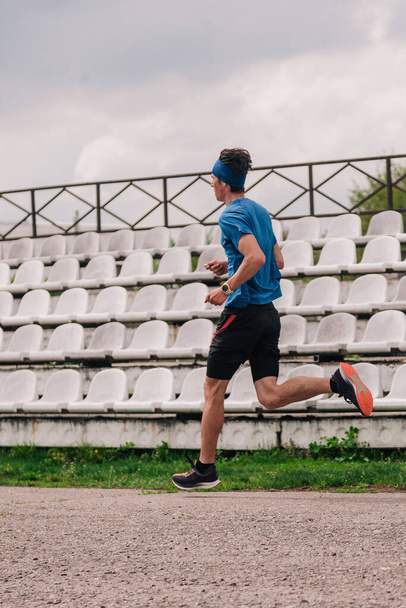 A young athlete in a blue T-shirt runs around the stadium - Fotografie, Obrázek