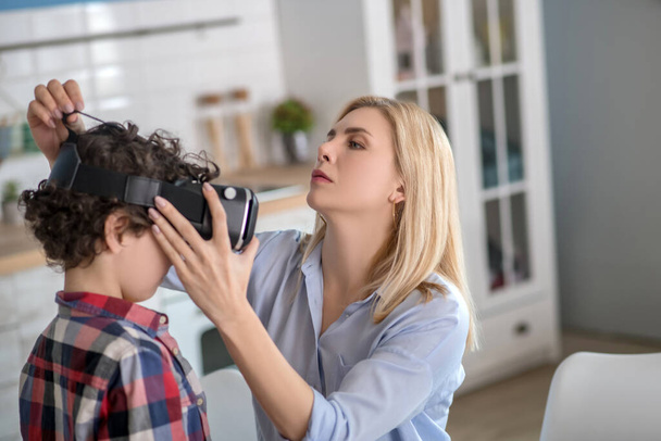 Blonde female putting on vr glasses on curly boy - Foto, afbeelding