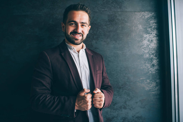 Portrait of cheerful caucasian male entrepreneur in trendy stylish outfit standing indoors enjoying luxury lifestyle, successful businessman dressed in stylish clothes posing near promotional backgroun - Foto, Bild
