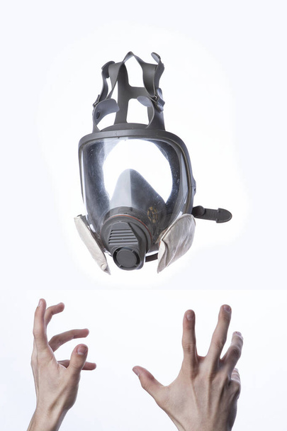 Hands reaching for a respirator on a white background. Respirator of the strengthened protection. The need for biological protection - Photo, Image