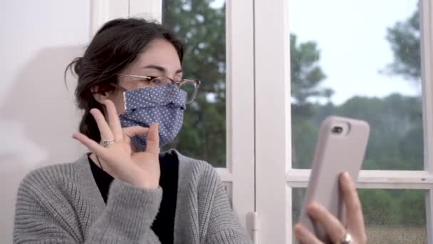 Coronavirus. Woman in quarantine for coronavirus wearing protective mask, she's working from home and using mobile phone at sofa. Video call. Video conference with mobile phone. - Filmagem, Vídeo