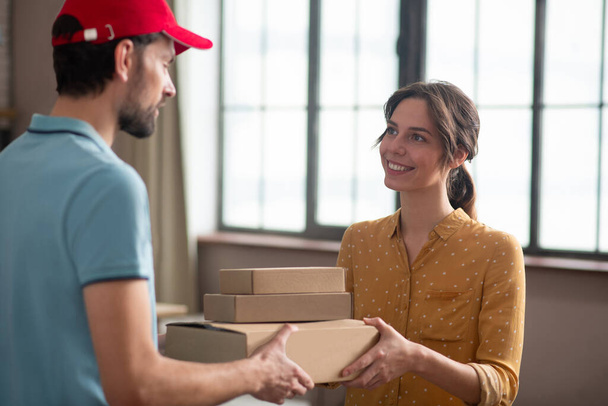 Female customer receiving boxes from a delivery person and looking contented - Foto, Imagen
