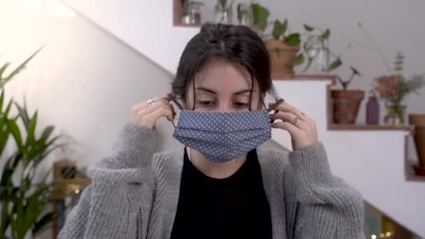 Woman putting on face mask at home. Quarantine young girl put on a fabric handmade mask.  - Séquence, vidéo