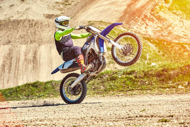 Motocross, a rider stands on the rear wheel of a bike, Riding on the rear wheel. Extreme, industrial, motorcycle cross-country riding for extreme. - Photo, Image
