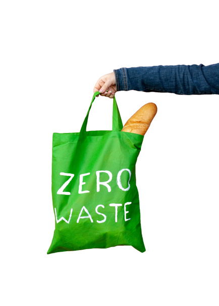 Groene eco tas met een witte tekst nul afval in de hand geïsoleerd op witte achtergrond. Frans brood is zichtbaar in de tas. Verticaal. - Foto, afbeelding