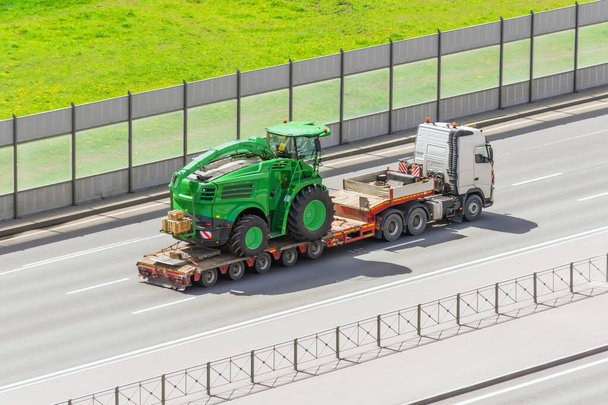 Transport maszyn rolniczych kombajn na przyczepie platformy załadunkowej ciężarówki na autostradzie w mieście - Zdjęcie, obraz