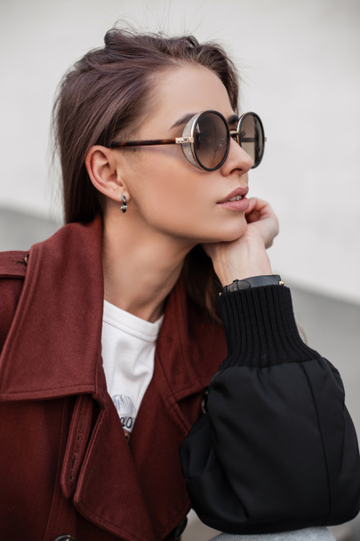 Cool stylish young woman model in brown fashion trench coat in sunglasses near wall on street. Fresh portrait american girl. Fashionable clothes for women. Spring casual look. Close-up female face - Foto, immagini