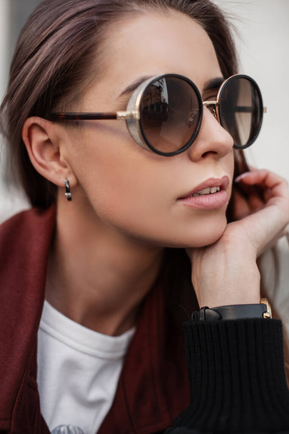 Portrait pretty european young woman with sexy lips with healthy skin in stylish sunglasses in fashionable brown trench coat. Beautiful girl model outdoors. Trendy clothes and accessories for women. - Foto, Bild
