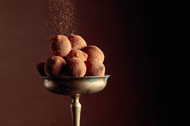 Chocolate truffles in old brass vase sprinkled with cocoa powder. Copy space. - Zdjęcie, obraz